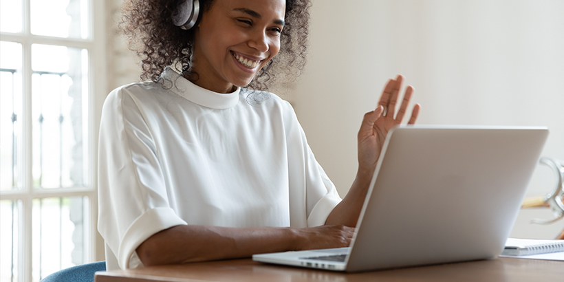 Photograph of a sales leader wearing headphones waving on a video call