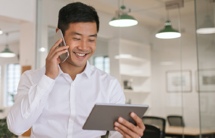 Photograph of a smiling revenue professional talking on a phone and looking at a tablet
